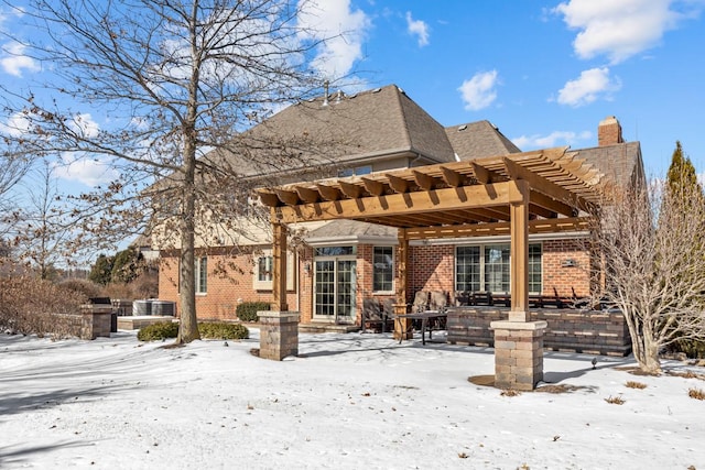 snow covered property featuring brick siding and a pergola