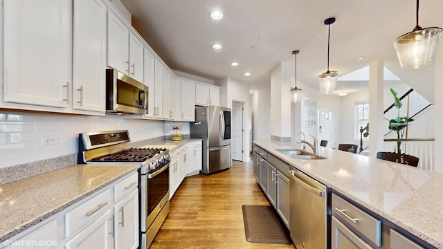 kitchen with tasteful backsplash, a sink, light wood-type flooring, appliances with stainless steel finishes, and white cabinetry