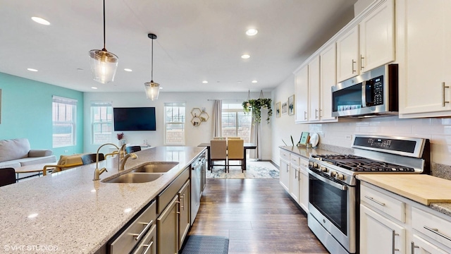 kitchen featuring tasteful backsplash, open floor plan, dark wood-style floors, appliances with stainless steel finishes, and a sink