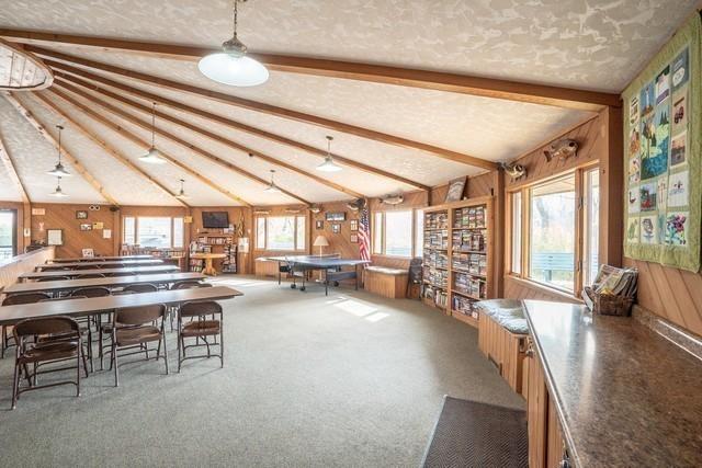 unfurnished dining area with carpet, vaulted ceiling with beams, wooden walls, and a textured ceiling