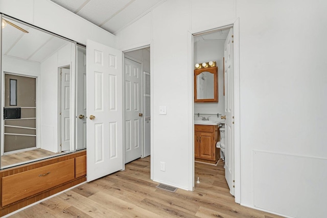 unfurnished bedroom featuring attic access, visible vents, lofted ceiling, ensuite bath, and light wood-type flooring