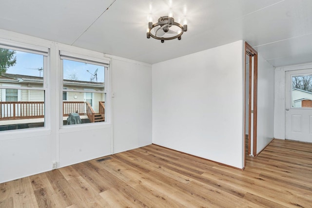 unfurnished room featuring light wood-style floors, visible vents, and a notable chandelier