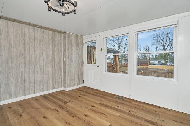 unfurnished room featuring a wealth of natural light, wood finished floors, visible vents, and wooden walls