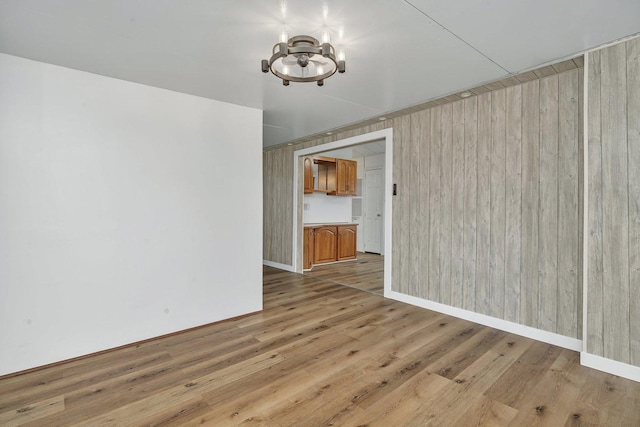 spare room featuring light wood-style floors, wooden walls, baseboards, and an inviting chandelier