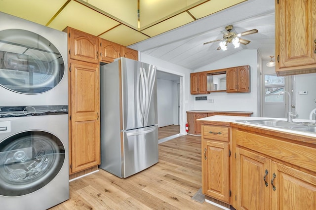 kitchen featuring freestanding refrigerator, stacked washer / dryer, vaulted ceiling, a sink, and light wood-type flooring