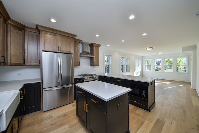 kitchen featuring dark brown cabinets, light wood-type flooring, a kitchen island, stainless steel appliances, and wall chimney range hood