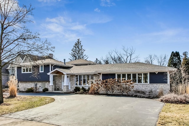 tri-level home with stone siding, driveway, and a chimney