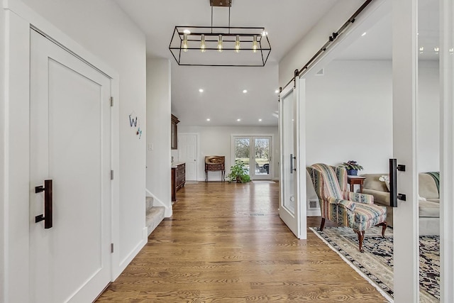 corridor with wood finished floors, visible vents, baseboards, recessed lighting, and a barn door