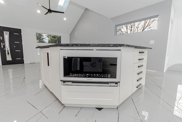 details featuring dark stone counters, white cabinets, ceiling fan, and a skylight