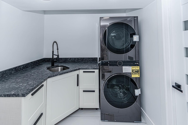 clothes washing area with stacked washer and dryer, cabinets, and sink