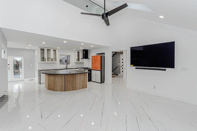 kitchen featuring wall chimney range hood, ceiling fan, a high ceiling, stainless steel range, and a kitchen island