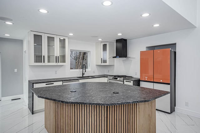 kitchen featuring sink, a center island, stainless steel range with gas stovetop, white cabinets, and wall chimney exhaust hood