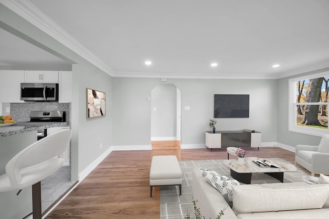 living area with baseboards, arched walkways, light wood-style flooring, ornamental molding, and recessed lighting