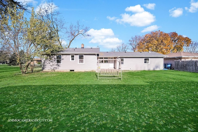 rear view of house with a chimney, fence, and a lawn