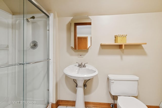 bathroom featuring toilet, a shower stall, and baseboards