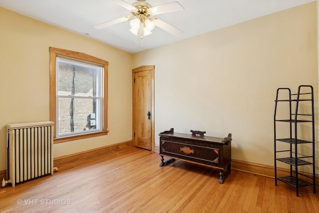 spare room featuring radiator heating unit, light wood-style floors, a ceiling fan, and baseboards