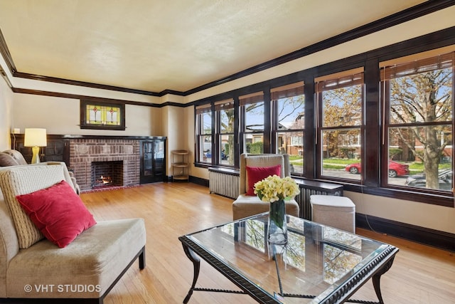 living area with baseboards, wood finished floors, crown molding, and a brick fireplace