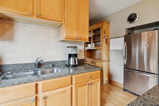 kitchen featuring dark stone counters, decorative backsplash, a sink, freestanding refrigerator, and light wood finished floors