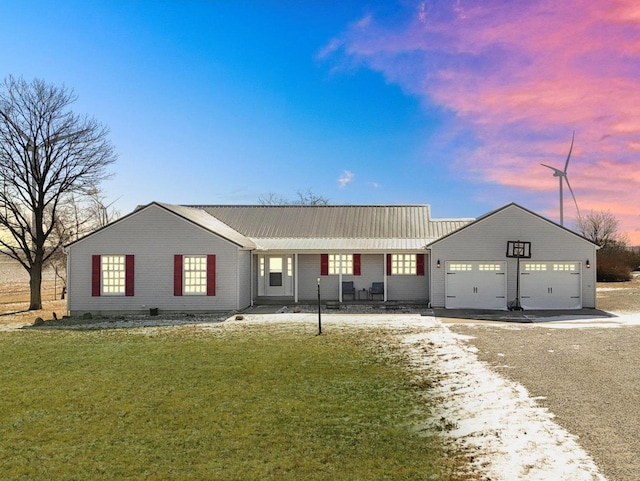 ranch-style house featuring a garage, metal roof, driveway, and a lawn