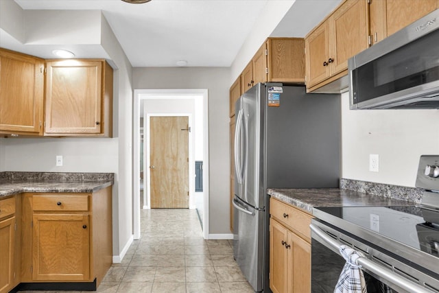 kitchen featuring light tile patterned flooring, stainless steel appliances, baseboards, brown cabinets, and dark countertops