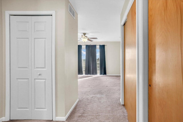 hallway with baseboards, visible vents, and light colored carpet