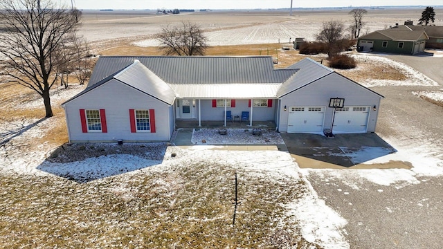 view of front of house featuring aphalt driveway, covered porch, an attached garage, metal roof, and a rural view