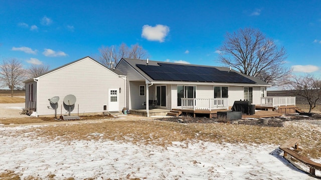 snow covered rear of property featuring a deck and roof mounted solar panels