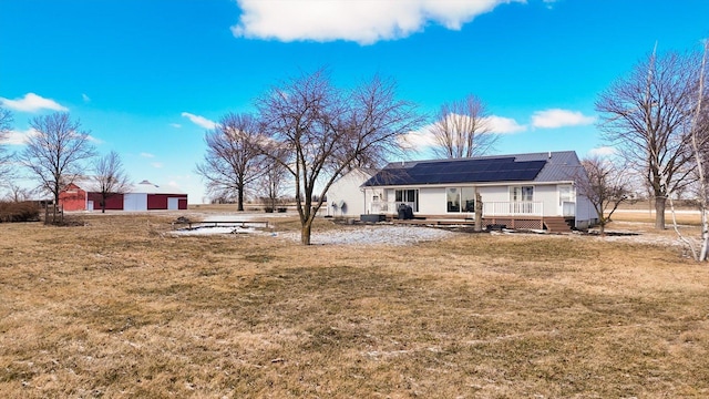 rear view of property with roof mounted solar panels, a yard, and a wooden deck