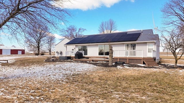 back of property with a lawn, metal roof, a deck, and solar panels