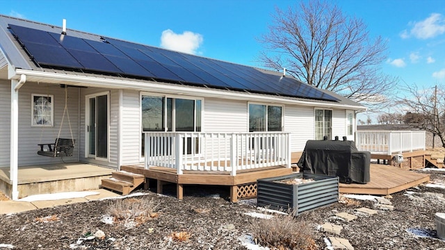 back of property with metal roof, roof mounted solar panels, and a deck