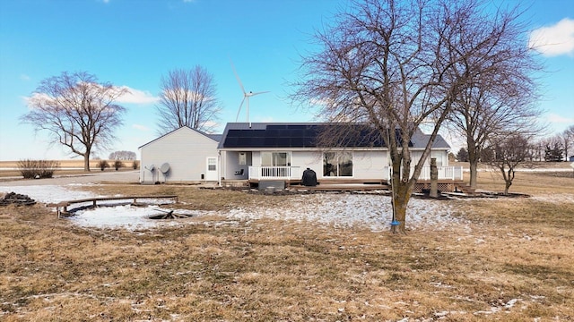 back of property featuring a lawn, a wooden deck, and solar panels