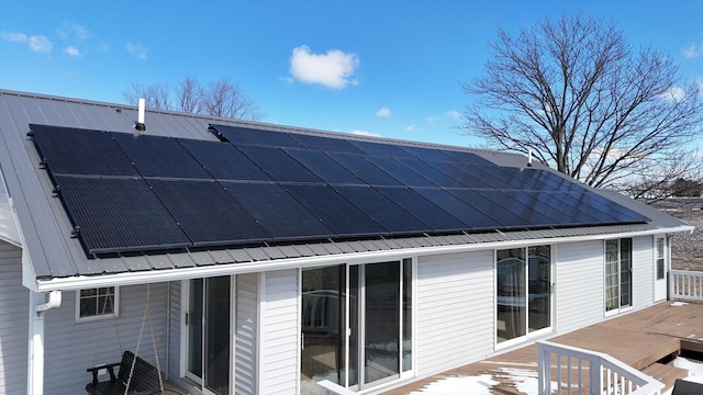 back of property featuring metal roof, solar panels, and a wooden deck