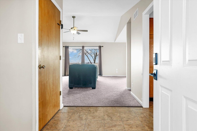 hallway featuring lofted ceiling, light colored carpet, visible vents, light tile patterned flooring, and baseboards