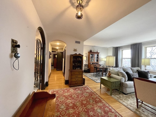 living area featuring arched walkways, visible vents, light wood-style floors, vaulted ceiling, and baseboards