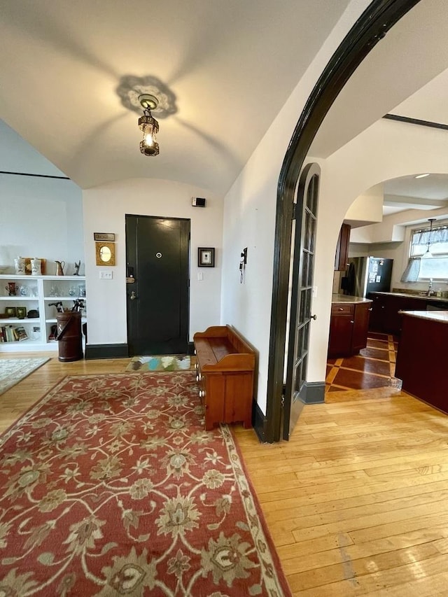 corridor with baseboards, arched walkways, lofted ceiling, light wood-style floors, and a sink