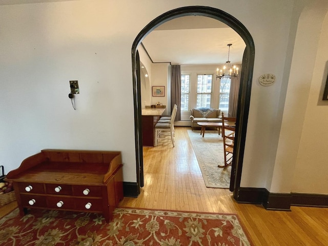 hall featuring arched walkways, baseboards, an inviting chandelier, and light wood-style floors