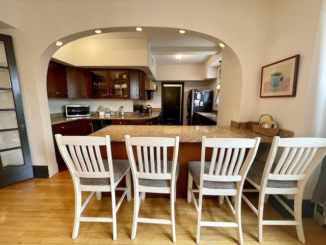 kitchen with a breakfast bar area, light wood-style flooring, a peninsula, freestanding refrigerator, and glass insert cabinets