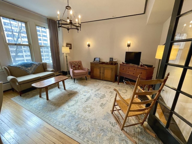 living area with a baseboard heating unit, light wood finished floors, and an inviting chandelier