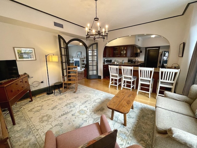 living area featuring a chandelier, arched walkways, visible vents, and light wood finished floors