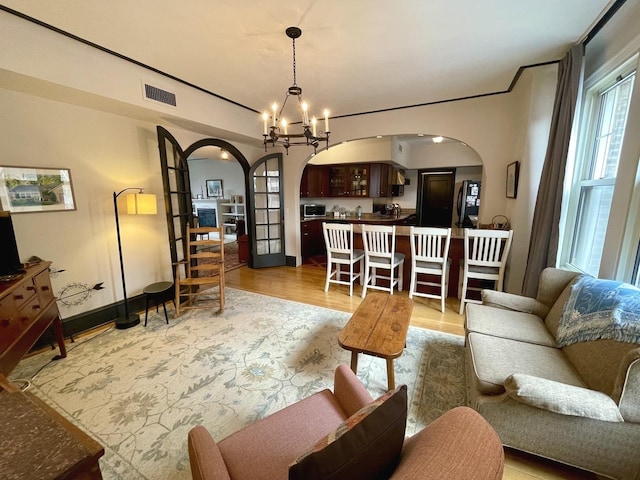 living area featuring light wood-style floors, arched walkways, a chandelier, and visible vents