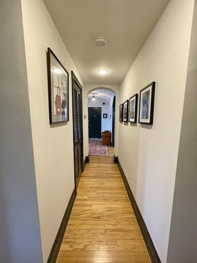 corridor with arched walkways, light wood finished floors, and baseboards