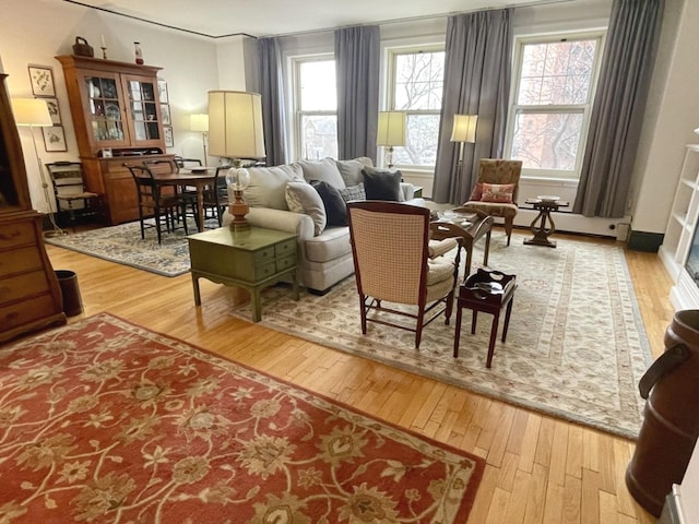 living area with baseboard heating, hardwood / wood-style flooring, and a healthy amount of sunlight