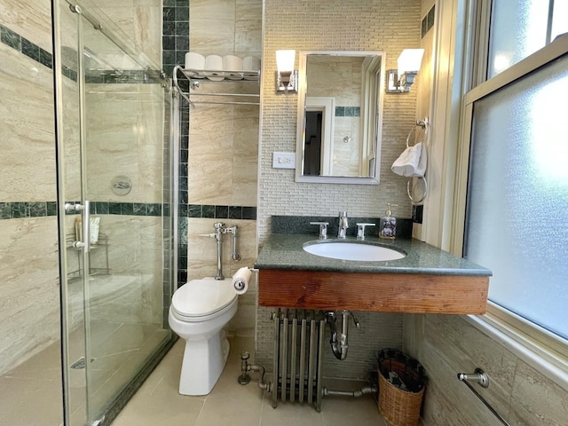 bathroom featuring a stall shower, toilet, a sink, tile patterned flooring, and tile walls