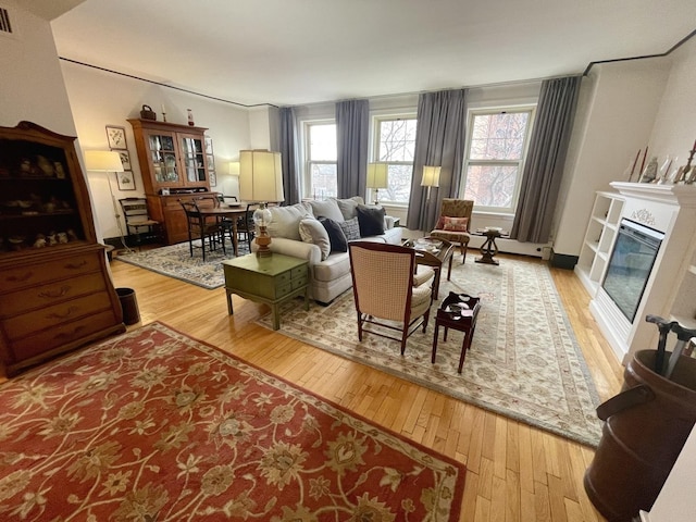 living room featuring visible vents, a glass covered fireplace, and hardwood / wood-style flooring