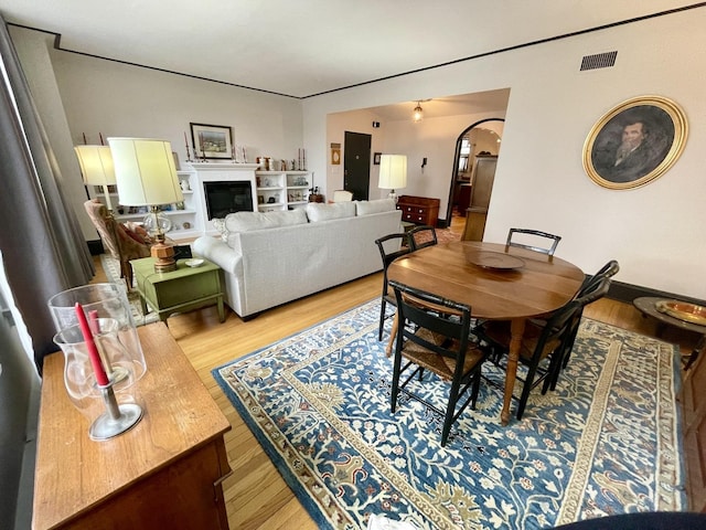 dining room featuring light wood-type flooring, arched walkways, visible vents, and a fireplace