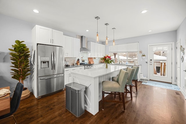 kitchen with stainless steel appliances, wall chimney range hood, dark wood-style flooring, and backsplash