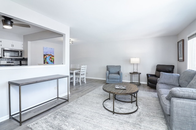 living area with wood finished floors, a ceiling fan, and baseboards