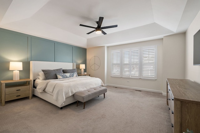 carpeted bedroom with a raised ceiling and ceiling fan