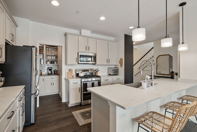 kitchen with appliances with stainless steel finishes, hanging light fixtures, light stone countertops, sink, and a kitchen bar