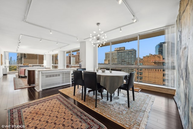 dining area with dark hardwood / wood-style flooring, rail lighting, a chandelier, and a wall of windows